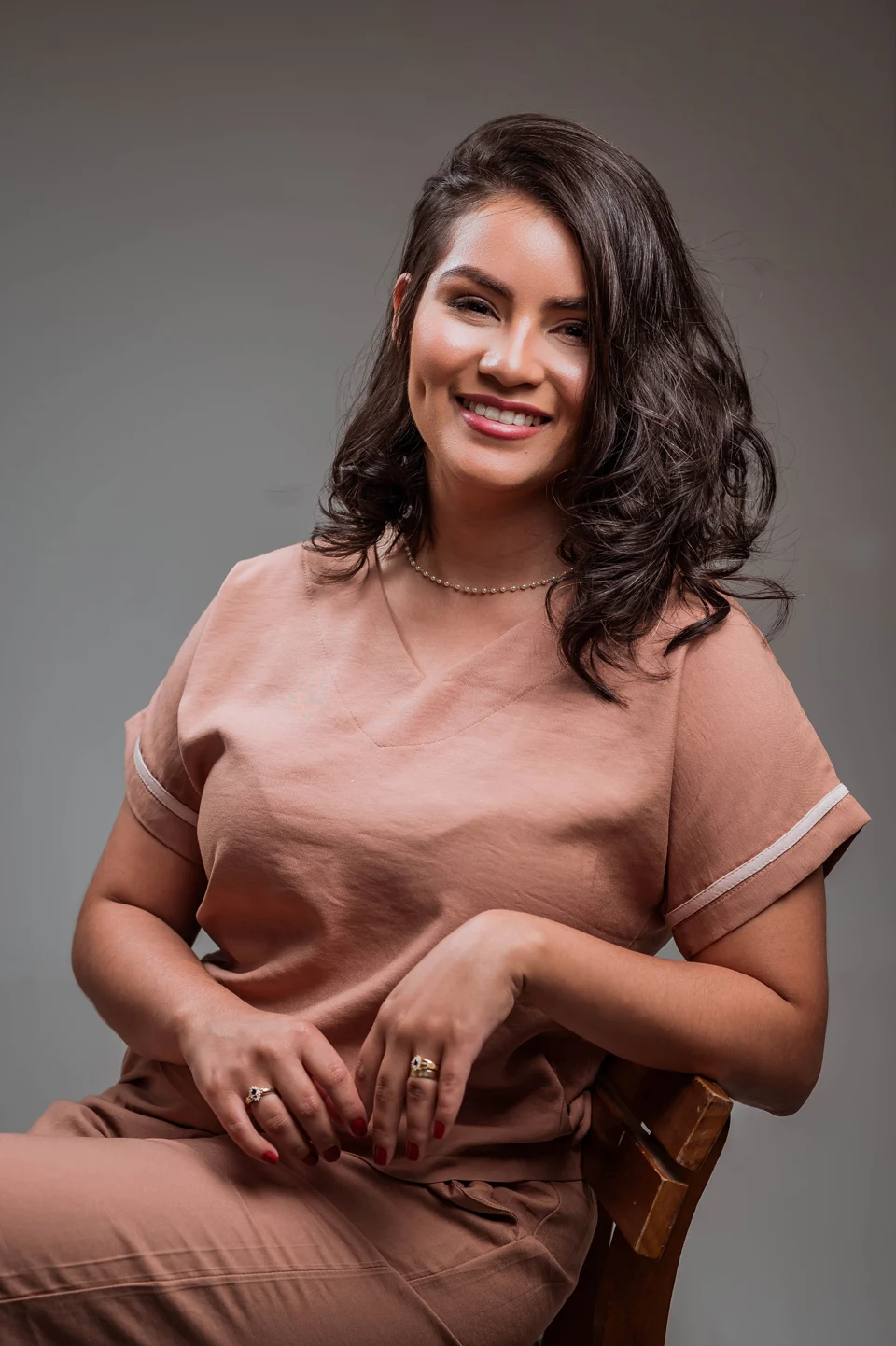 Nicolly Cabral sorrindo, sentada, com roupa em tom neutro